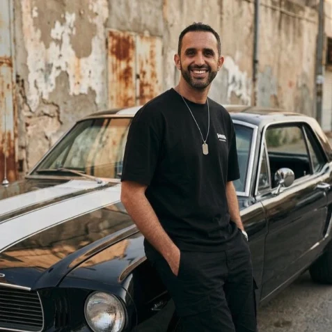 Alex Spitz, apoyado en un auto clásico negro, sonriendo de frente